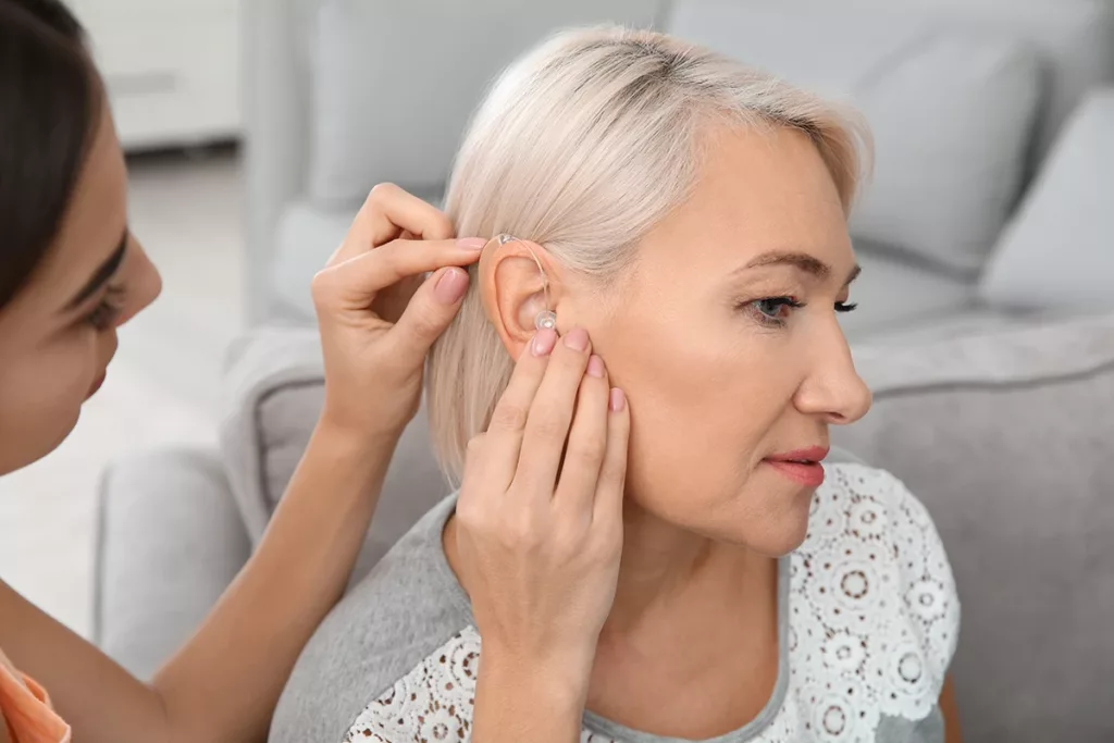 Young woman thoughtfully putting hearing aid in mother's ear.