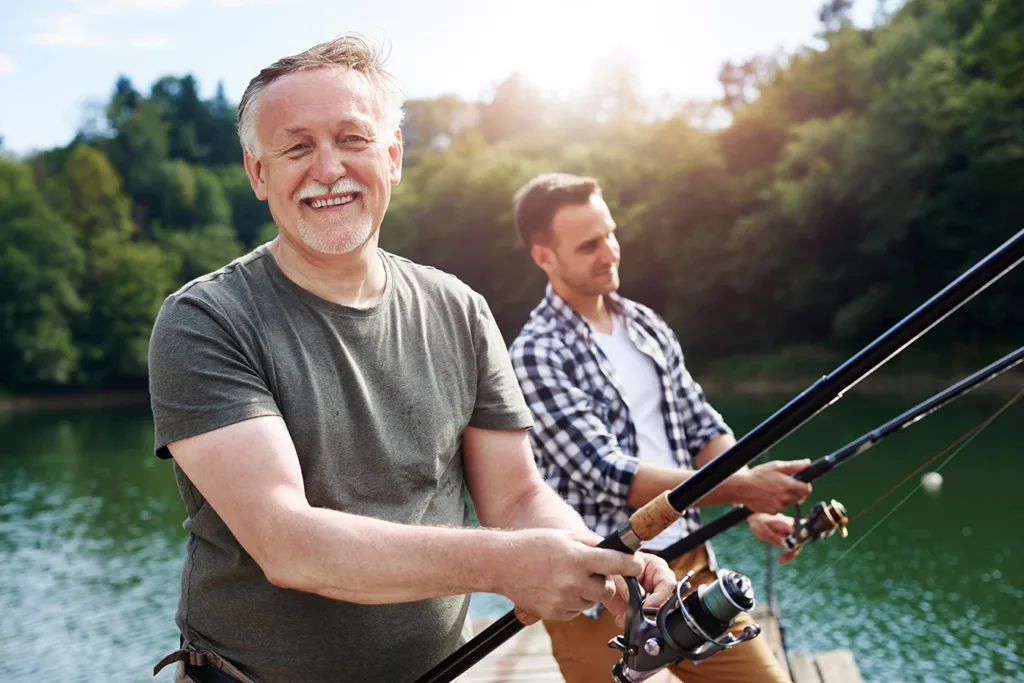 A mature man with his son standing on a dock finish in a beautiful blue lake, symbolizing Advanced Hearing Aid Durability and Reliability in 2026